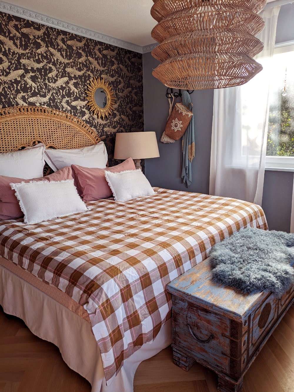 Bett mit Rattankopfteil vor Fischtapete. Eine blaue indische Truhe steht am Fußende des Bettes.
